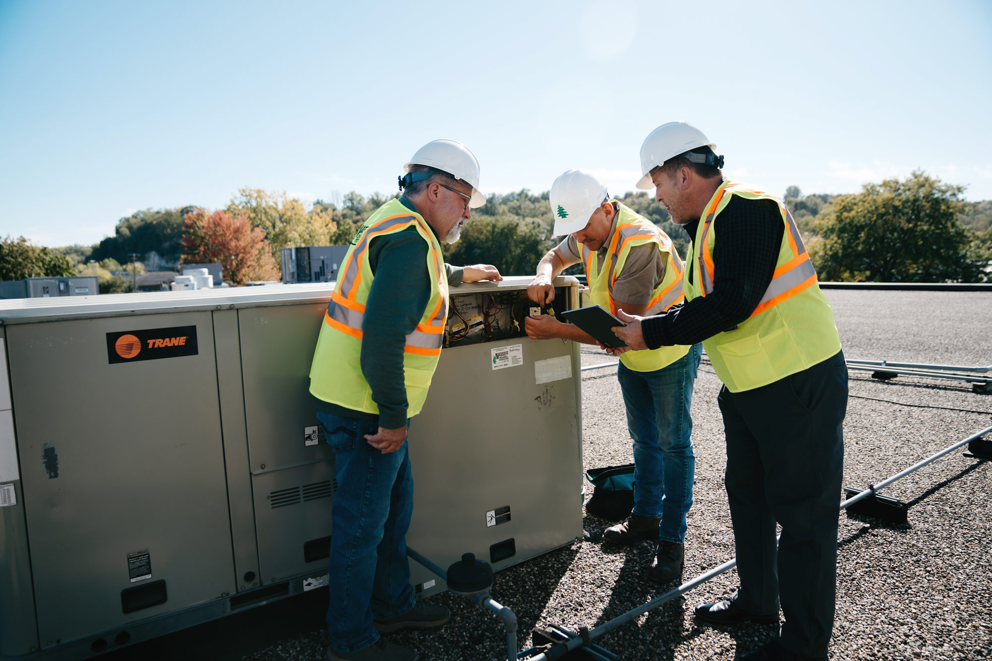 workers in yellow safety vests working on a mechanical unit on a roof