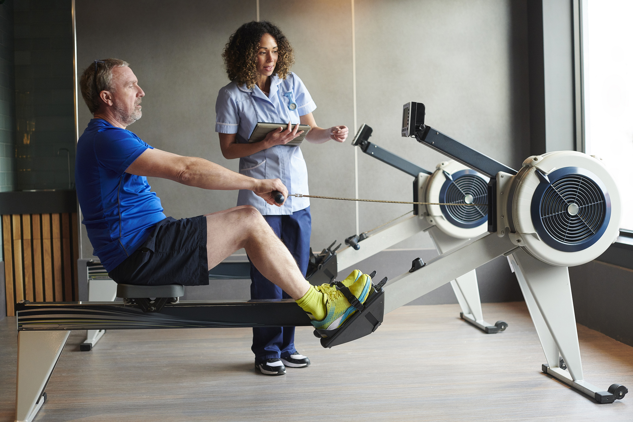 Man on rowing machine being instructed by woman doctor